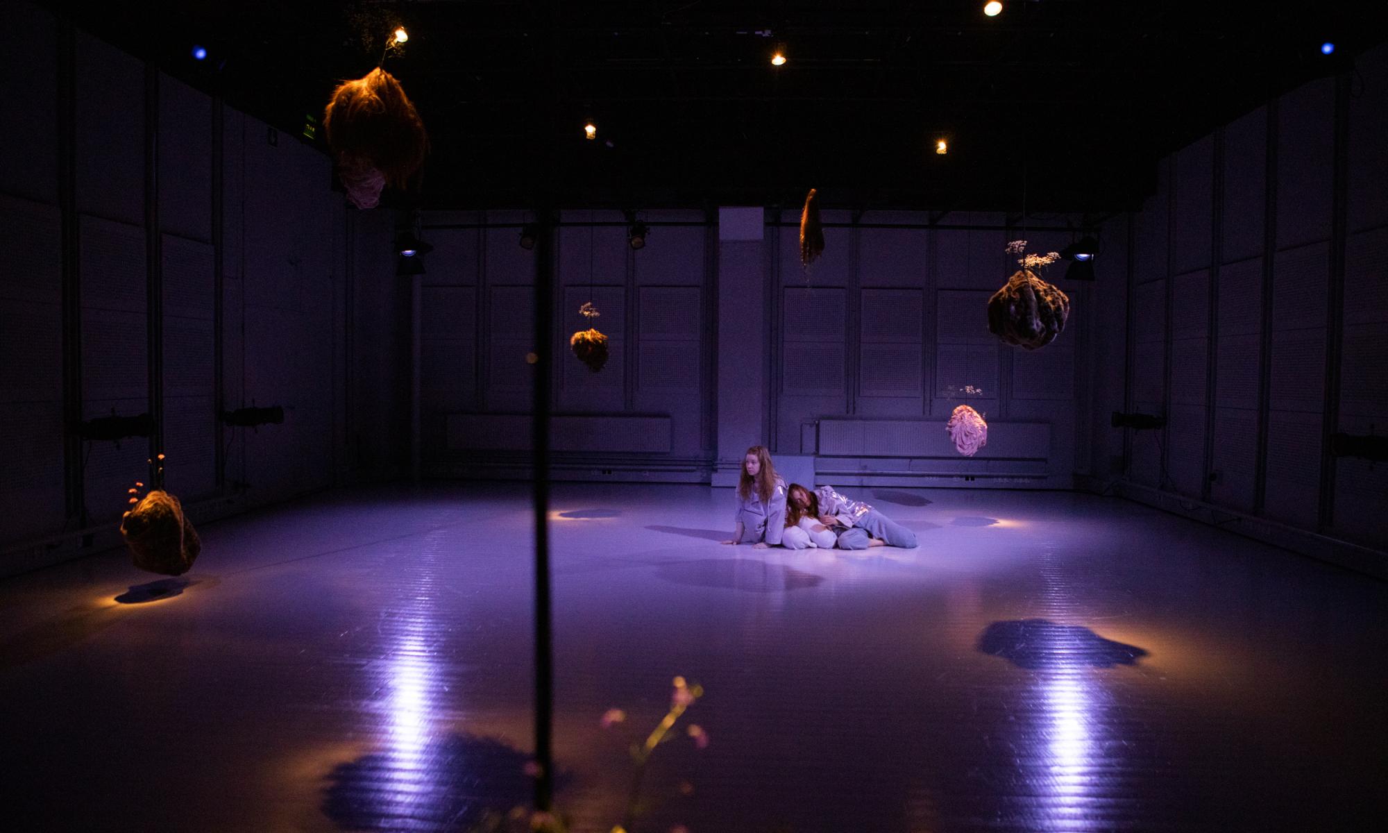 Purple light white box performance space with two performers.