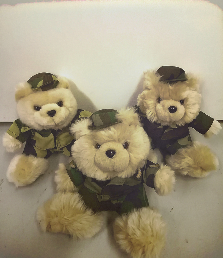 Kolme vaaleaa pehmokarhua maastokuvioisissa armeijatakeissa ja -hatuissa