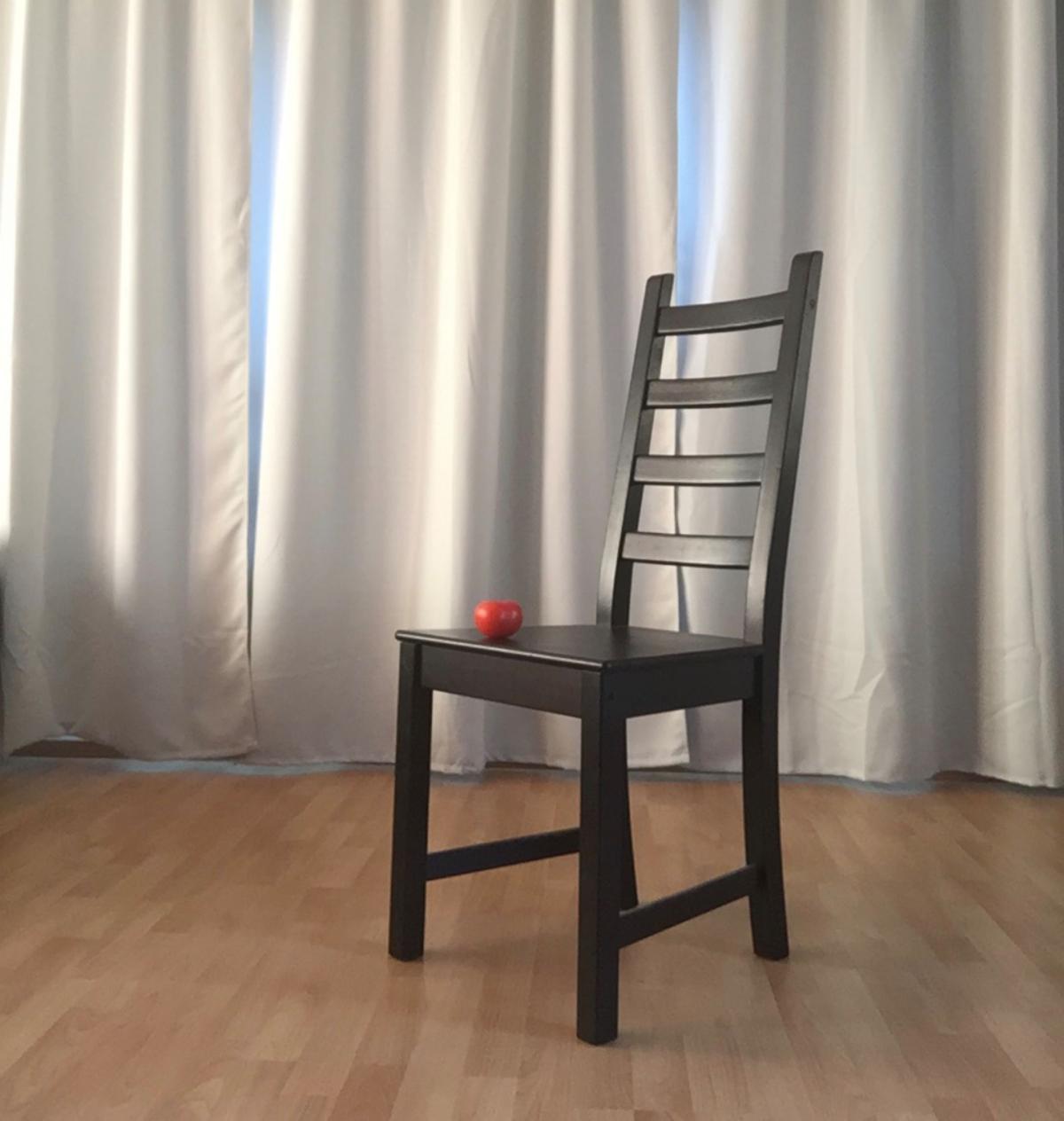 Tuoli harmaan verhon edessä, tuolilla tomaatti