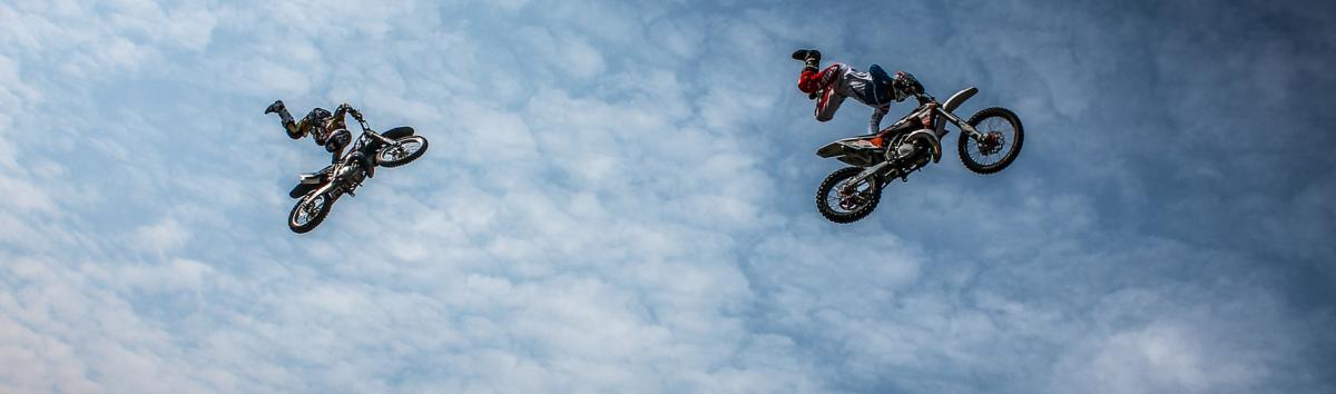 Moottoripyöräilijät tekevät ilmalentoa. Kuva otettu alhaalta päin.