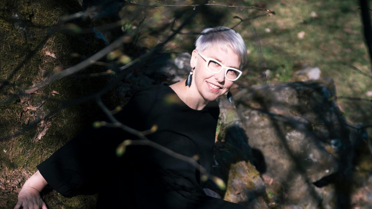 Dosentti Raisa Foster istuu ulkona ja katsoo kameraan.