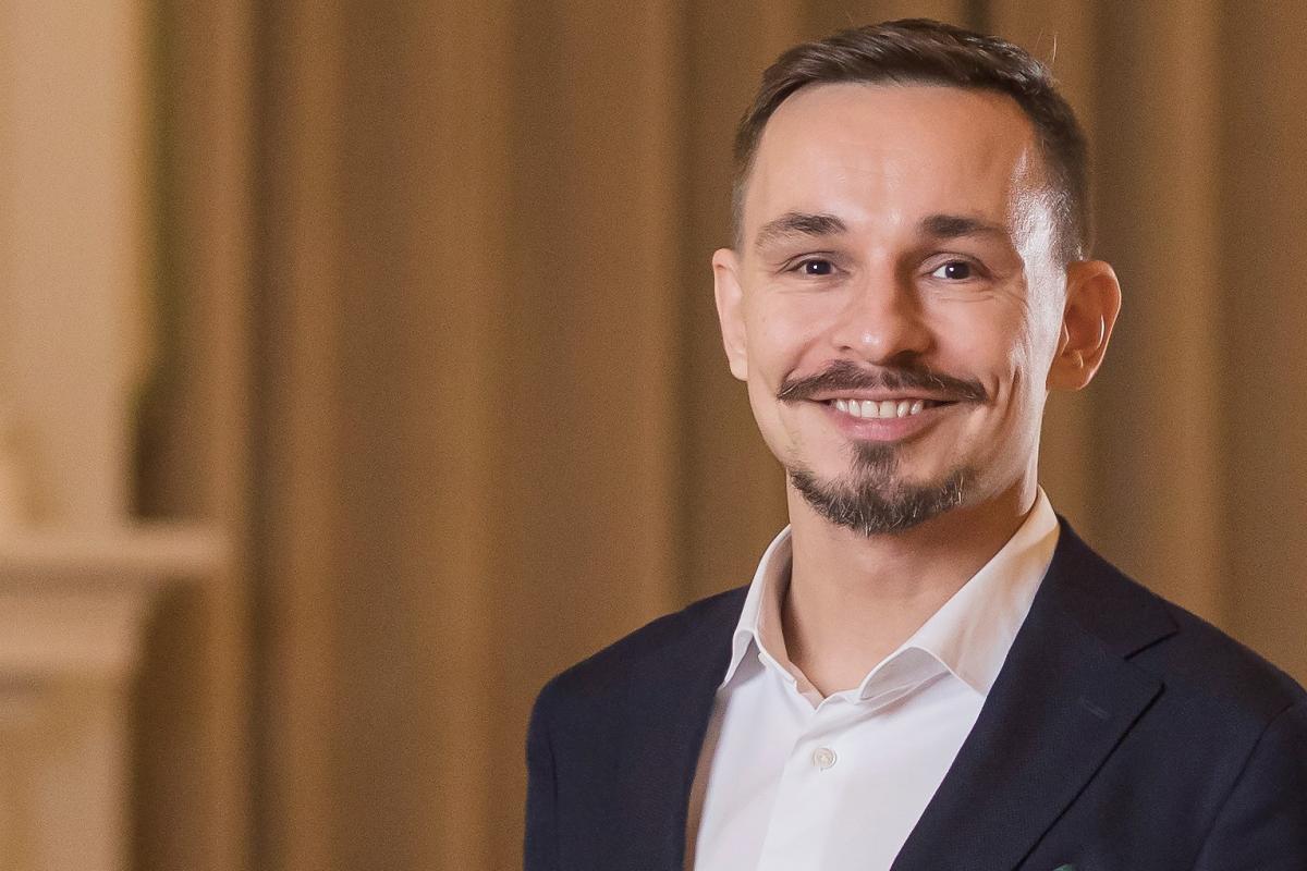 Tommi Laitio hymyilee kameralle. Kuva on otettu sisätiloissa. Tausta on neutraalin värinen