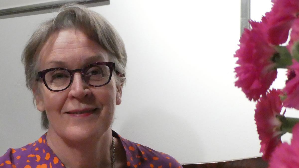 Eija Kauppinen hymyilee kuvassa valkoisen seinän edessä. Päällä hänellä on punainen paita