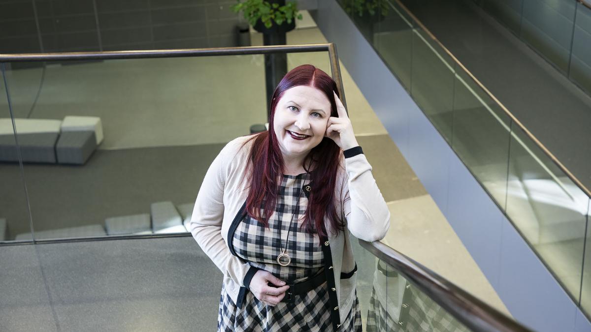 Heidi Lehmuskumpu nojaa kädellään porraskaiteeseen Musiikkitalon portaikossa ja hymyilee kameralle.