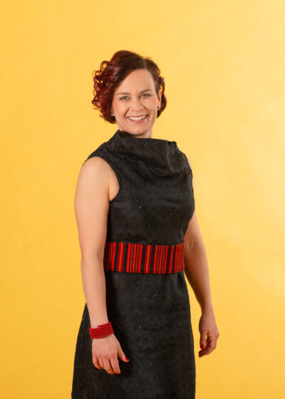 Sirpa katsoo iloisena suoraan kameraan. Kuvassa vain hän keltaisella taustalla.