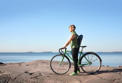 Emilia seisoo merenrantakalliolla pyöränsä kanssa viulukotelo selässä.