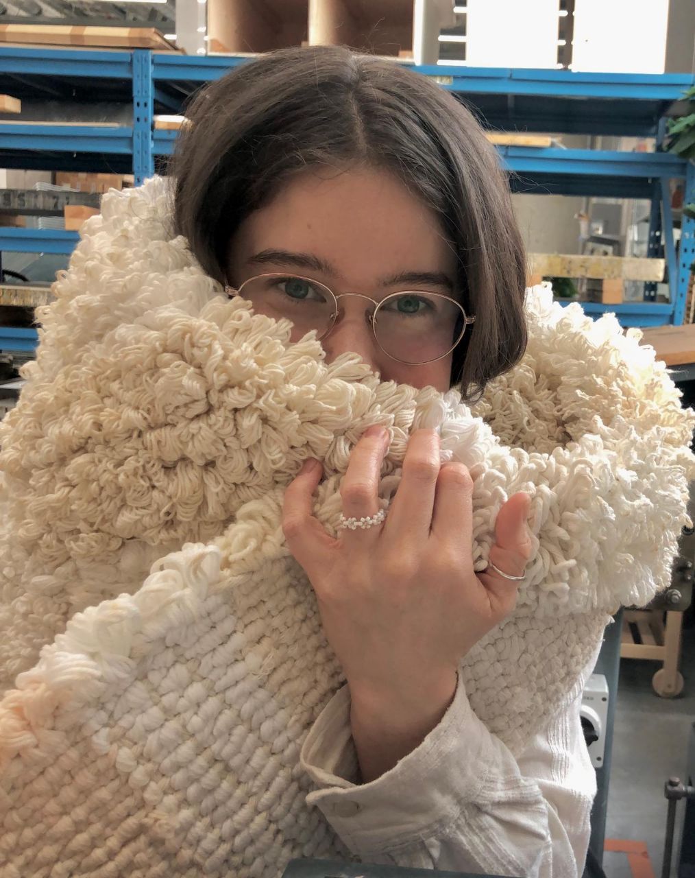 A picture of Elle, a brown haired white woman with glasses and a fluffy white rug covering half of her face