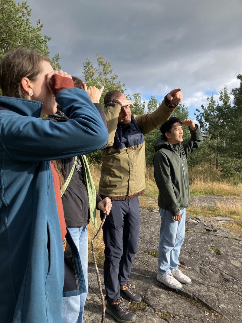Four people standing on a wide rock, pointing at something they are looking at.