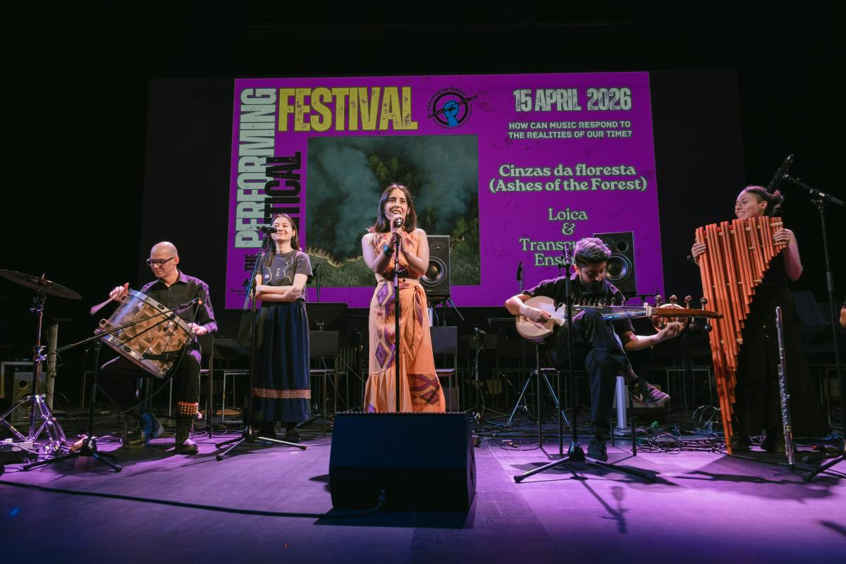 A band on the stage with Performing the political screen on the background.