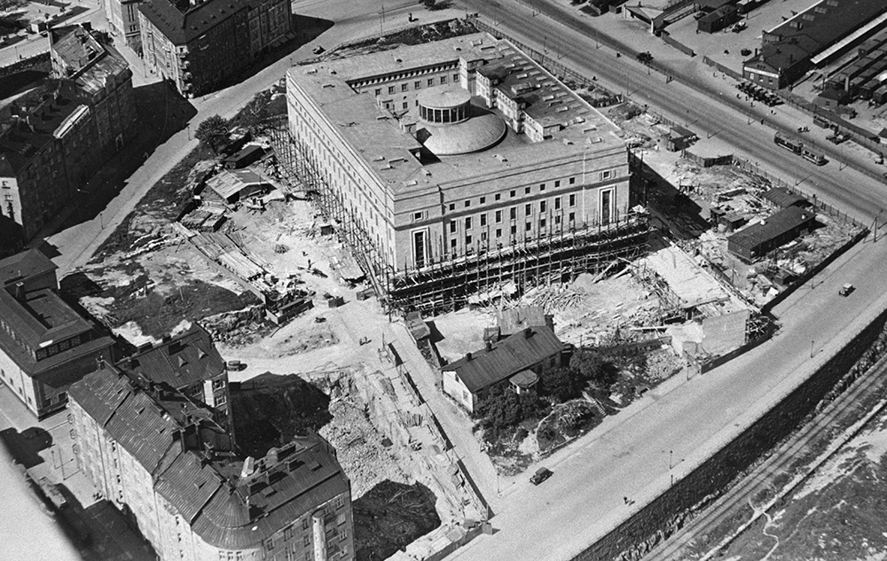 Flygbild av byggandet av riksdagshuset och dess miljö 1930. Nere på bilden syns konservatoriebyggnadens tomma tomt där berget sprängts. 