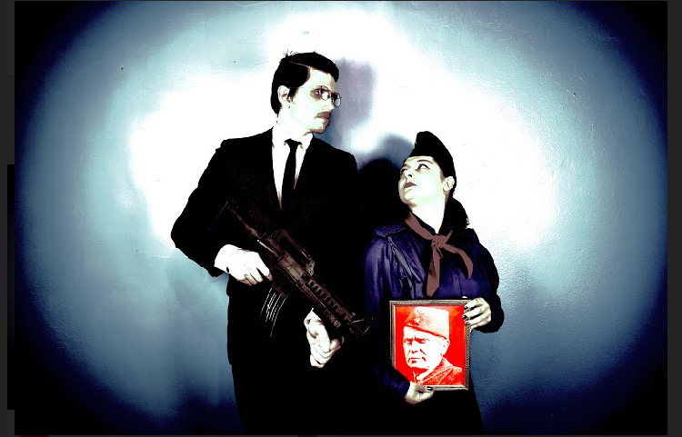 The Missing Torch video performance promo image with Fjolla Hoxha as the Adult Pioneer, wearing a pioneer uniform and holding a riso printed image of Tito, the leader of ex-Yugoslavia and Dylan Simon as the Travel Agent in a suit, holding a machine gun. They are looking at each other. 