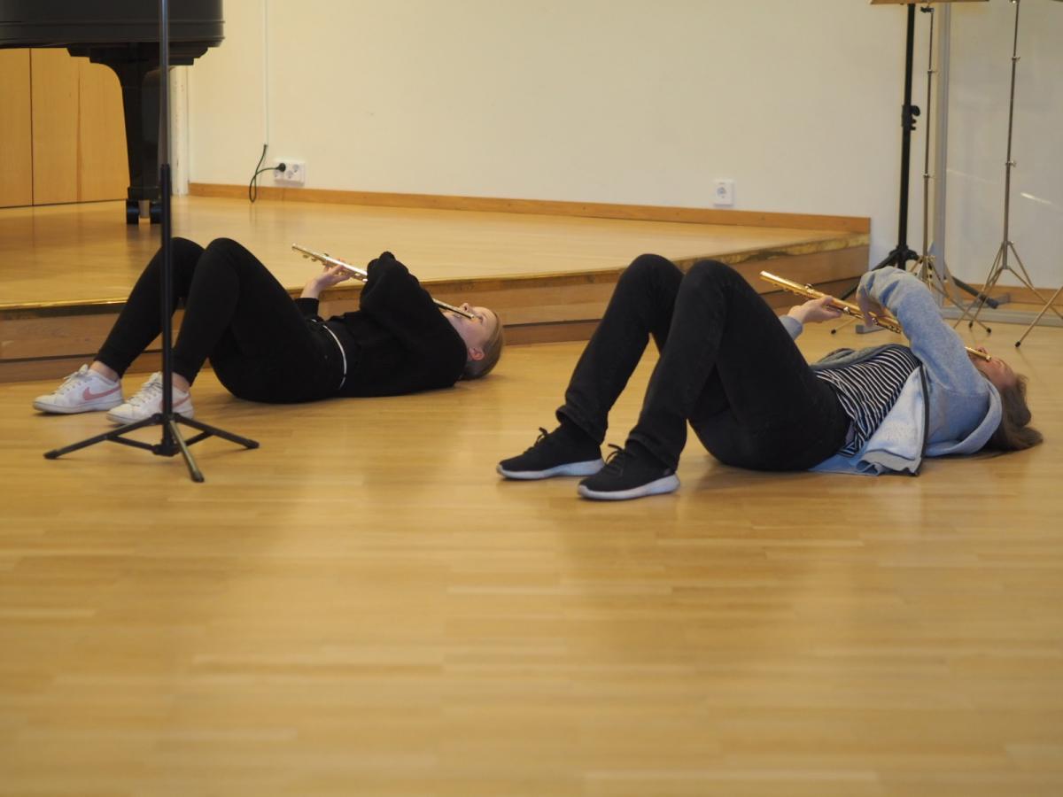 Opettaja Hanna Kinnunen ja huiluopiskelija makaavat luokkahuoneen lattialla harjoittelemassa soittoasentoa