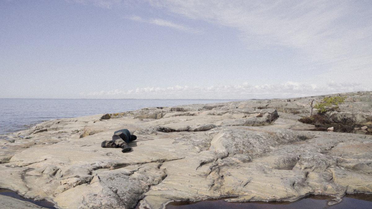 A person lying down on a rocky seashore.