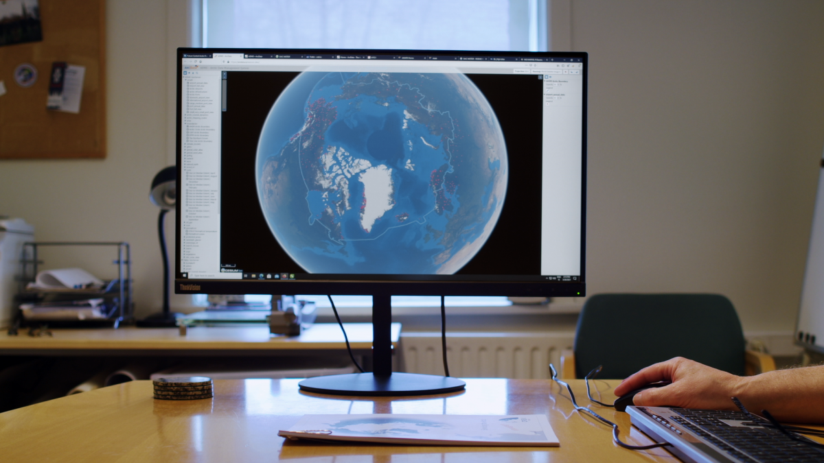 A screen on a table with a picture of the globe and a typing white skinned hand on the right.
