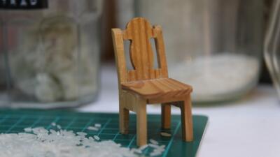 A tiny wooden chair sitting on a studio desk with some rice
