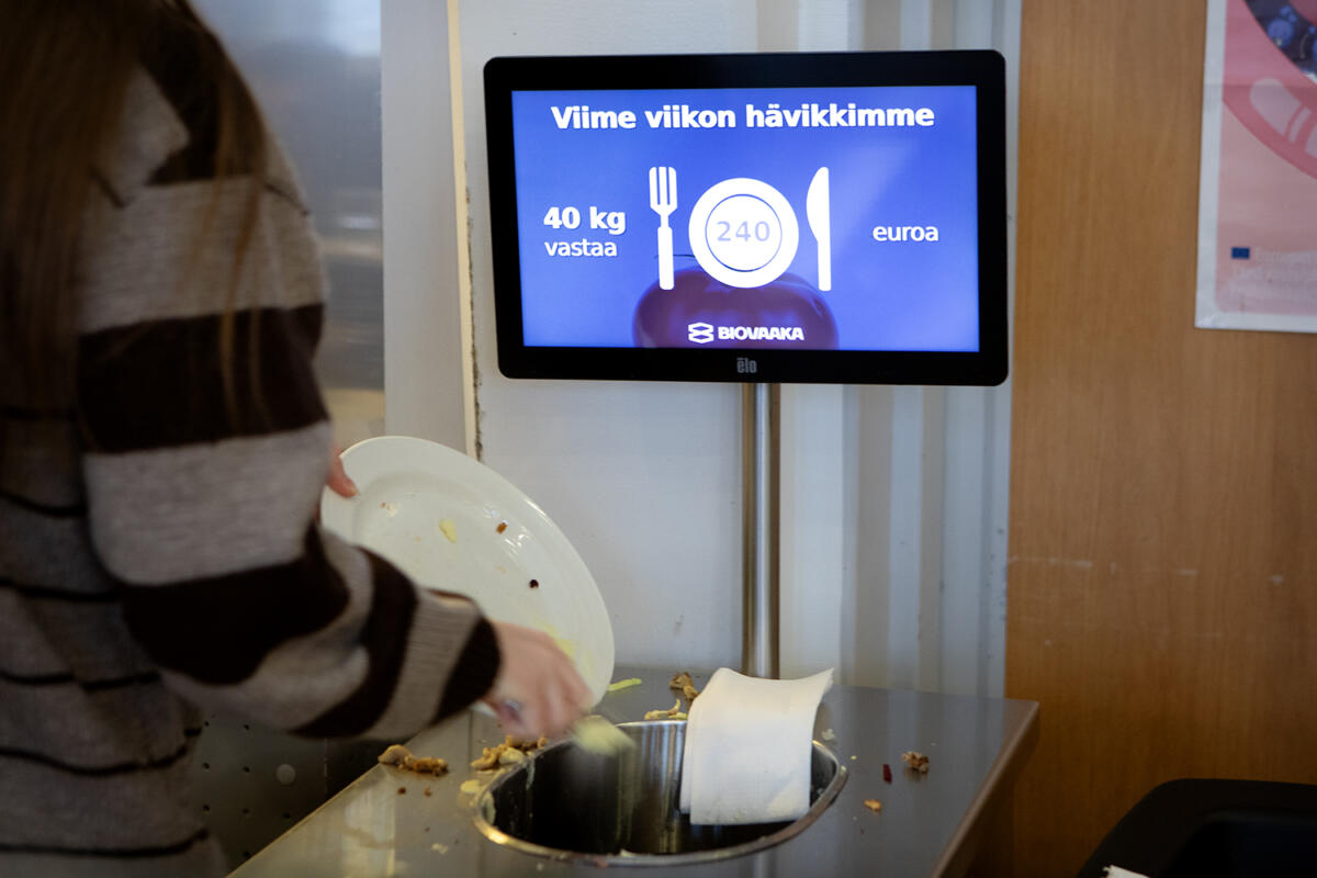 Kuvassa hävikkivaa'an edessä koululainen tyhjää lautastaan biojätteeseen.